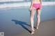 A woman in a pink bikini walking on the beach.