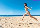 A woman in a bikini jumping in the air on a beach.