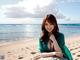 A woman in a green dress sitting on a rock on the beach.