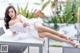 A woman in a white dress sitting on a table by a pool.